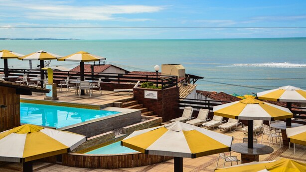 A pool area with umbrellas, lounge chairs, and a view of the ocean. - Flat Pipa Oceano (Tibau do Sul)