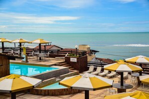 A pool area with umbrellas, lounge chairs, and a view of the ocean. - Flat Pipa Oceano (Tibau do Sul)