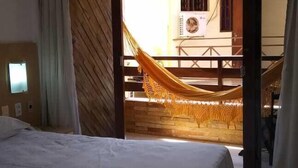 A hotel room with a bed, a window, and a view of an outdoor area with a hammock. - Flat Pipa Oceano (Tibau do Sul)