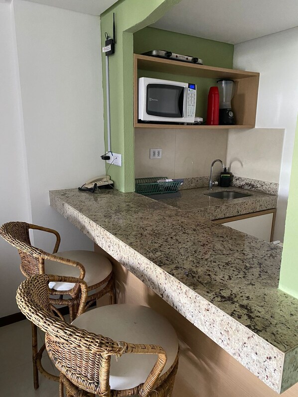 A compact kitchen with a granite countertop, a microwave, a sink, and wicker chairs. - Flat Pipa Oceano (Tibau do Sul)