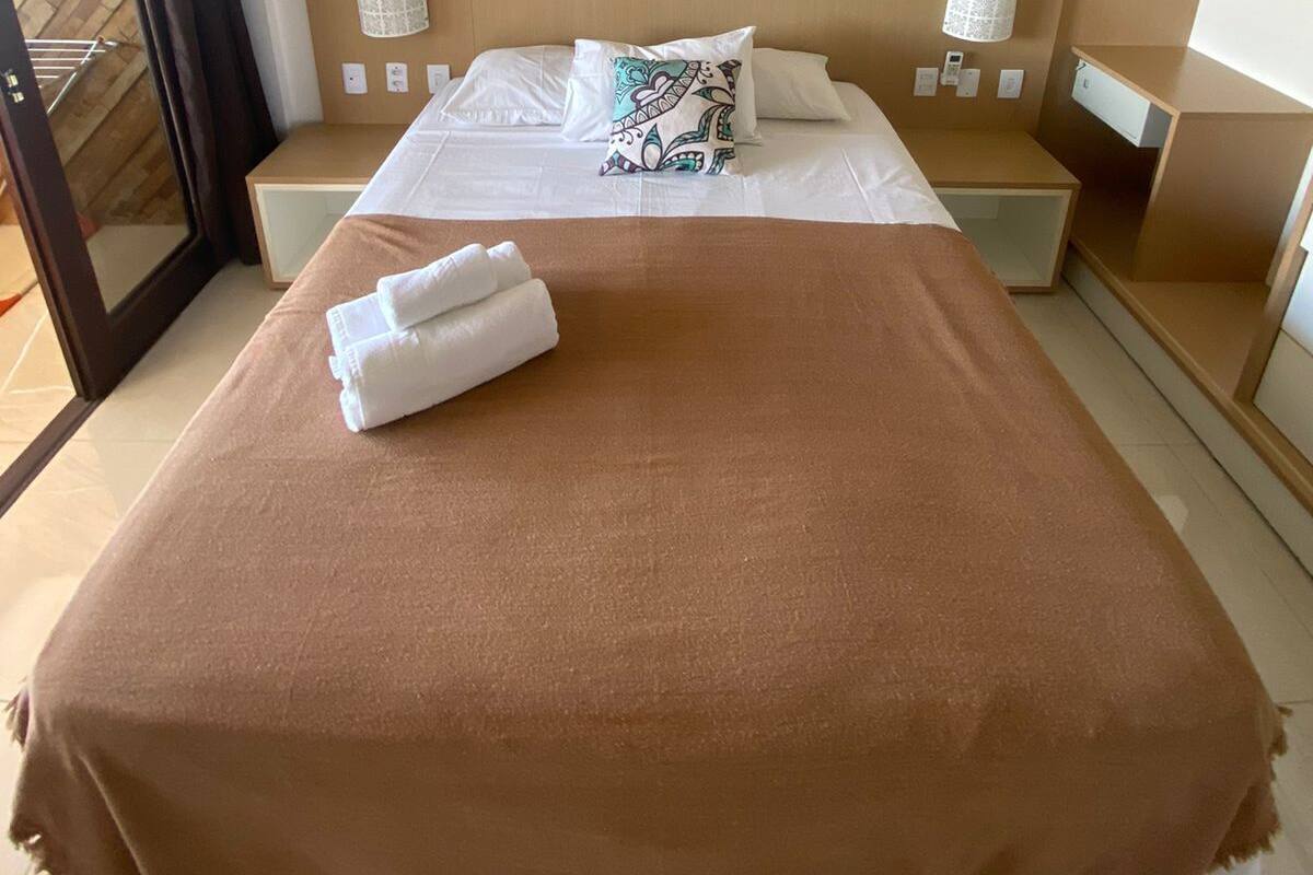 A hotel room with a bed, a bedside table, a nightstand, a mirror, and a door to a balcony.