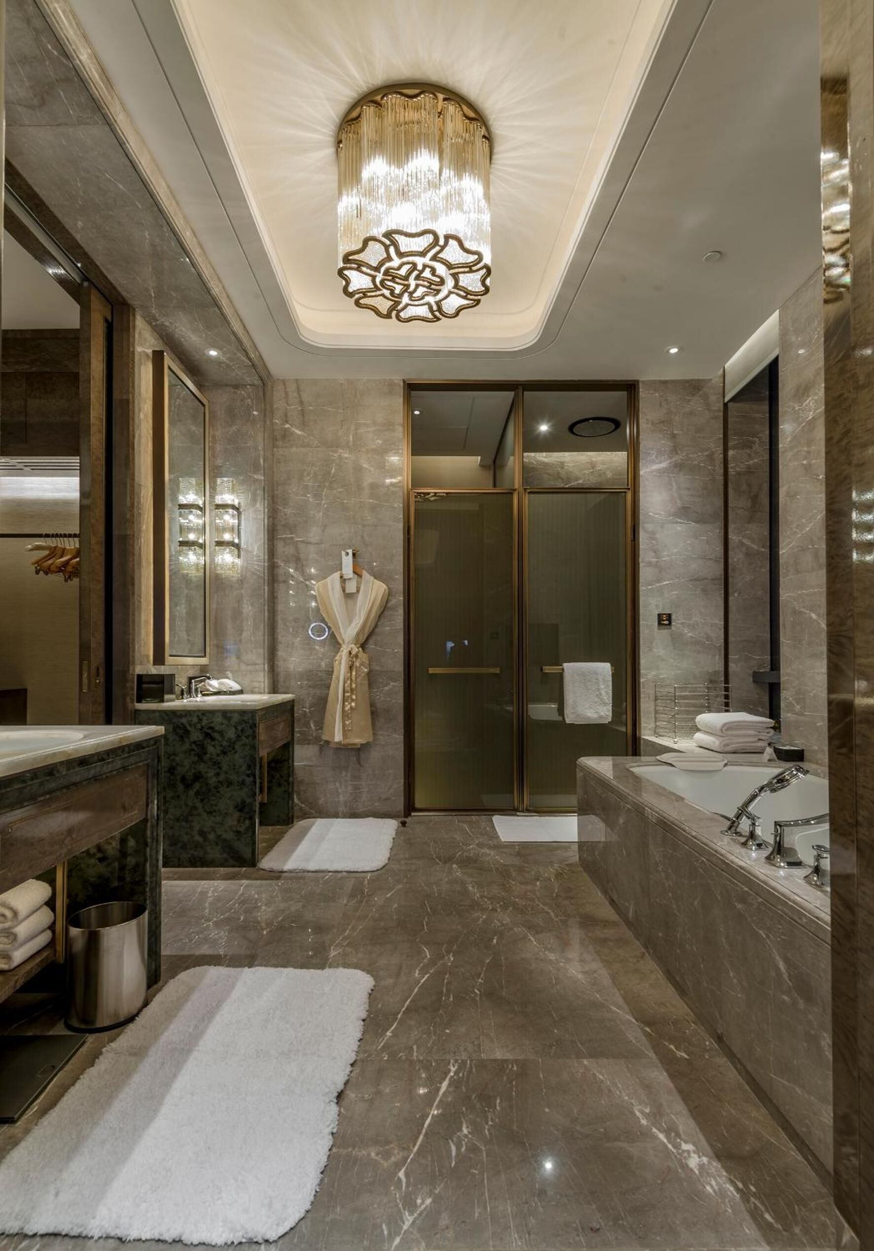 A luxurious bathroom with a large mirror, two sinks, a walk-in shower, and a chandelier.