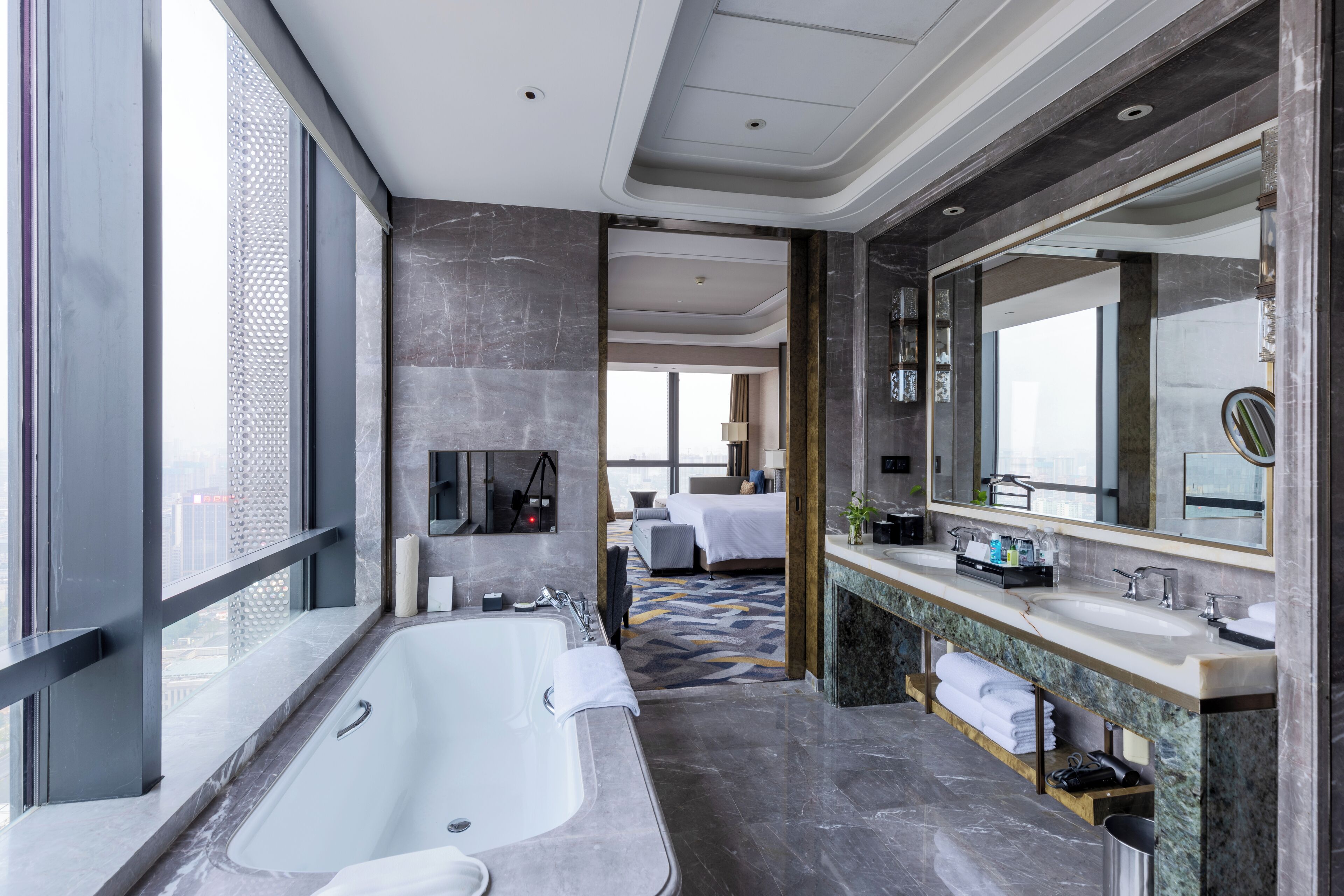 A modern hotel bathroom with a large bathtub, a double sink vanity, and a large mirror.