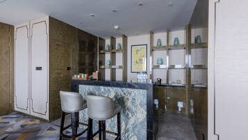 A modern kitchen with marble countertops, two bar stools, and decorative vases on shelves.