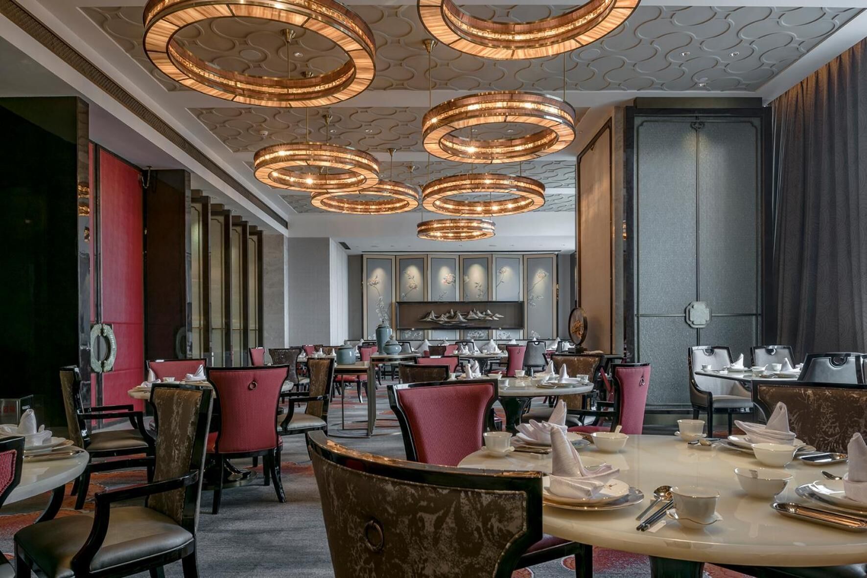 Un interior de restaurante con varias mesas y sillas para comer, lámparas decorativas en el techo y una pared con obras de arte enmarcadas.