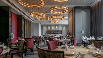 Un interior de restaurante con varias mesas y sillas para comer, lámparas decorativas en el techo y una pared con obras de arte enmarcadas.