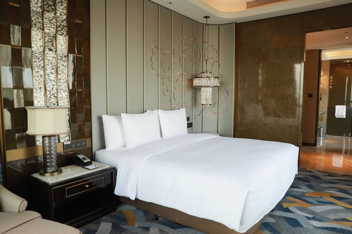 A hotel room with a large bed, a bedside table with a lamp, a telephone, and a chair.