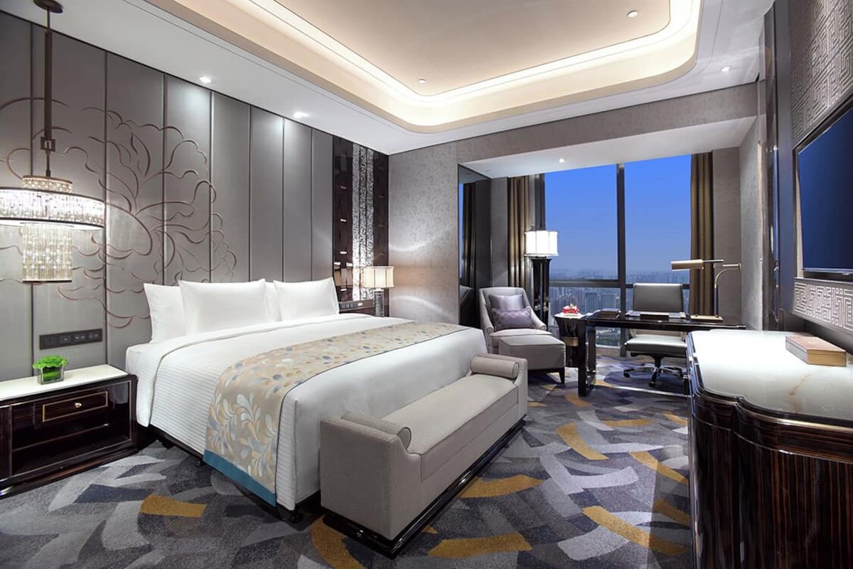 A modern hotel room with a large bed, a desk, and a TV.