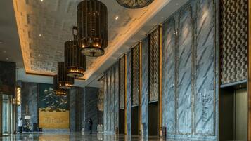 En rummelig lobby med et skinnende marmorgulv, et højtloft med geometriske mønstre og moderne lysekroner.
