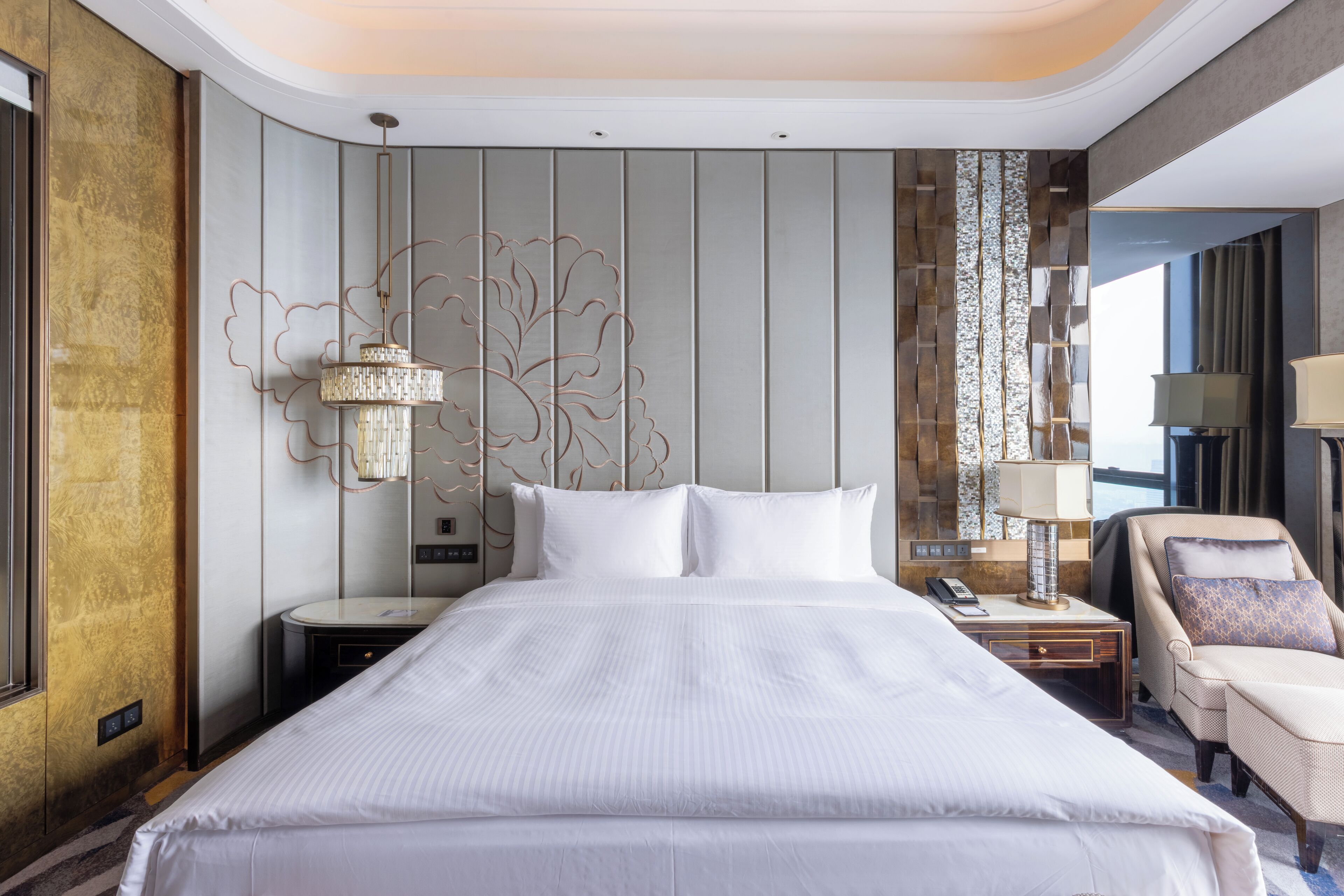 A hotel room with a large bed, a nightstand, a chair, and a decorative wall panel.