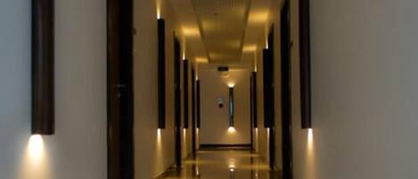 Un largo pasillo bien iluminado con piso reflectante, que conduce a una puerta al final.