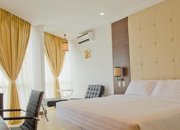 Habitación de hotel con una cama grande, una silla, un escritorio y aire acondicionado de pared.