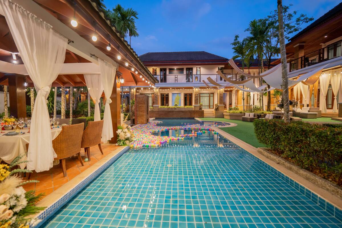A swimming pool with a tiled deck, surrounded by outdoor seating and a covered area with white drapes.