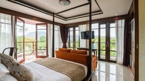 A spacious bedroom with a large bed, a seating area, and a balcony with a view of the mountains. - Jantra Residence by Chinocollection (Kathu)