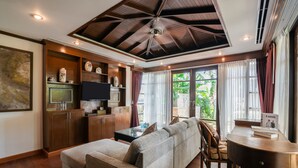 A modern living room with a sectional sofa, a flat-screen TV, wooden cabinets, and a ceiling fan. - Jantra Residence by Chinocollection (Kathu)