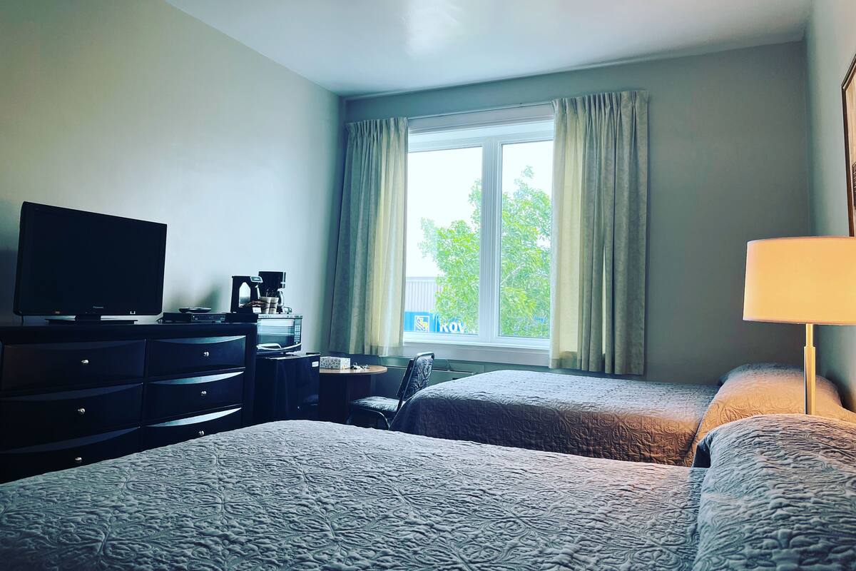 Habitación de hotel con dos camas, televisión, escritorio con cafetera y ventana con cortinas.