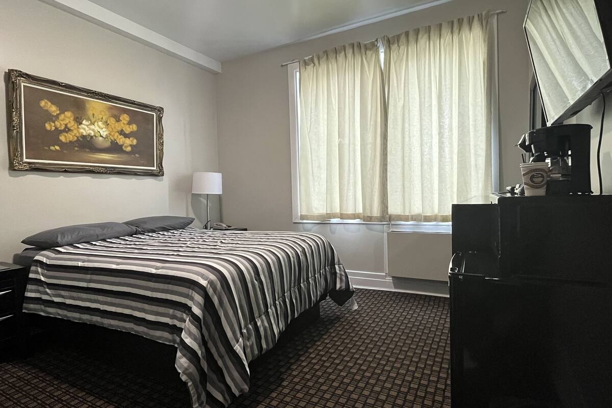 Habitación de hotel con cama, escritorio, lámpara, cafetera y ventana con cortinas.