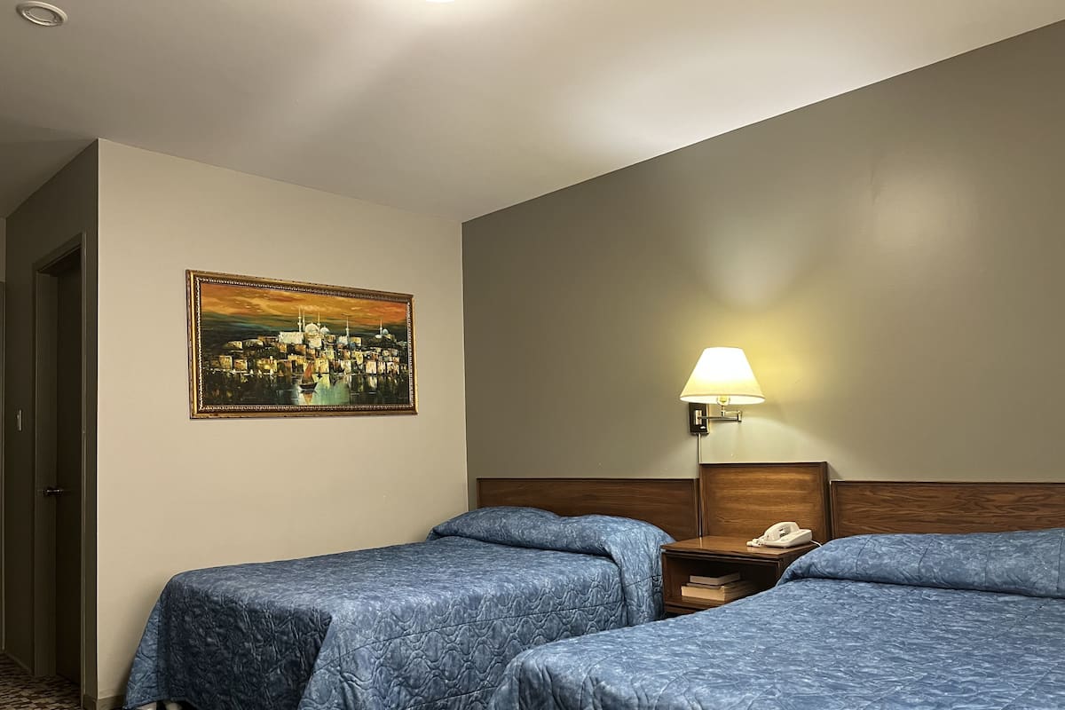 Una habitación de hotel con dos camas, una mesita de noche, una lámpara y un cuadro en la pared.