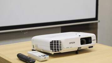 A white Epson projector on a wooden table with a remote control beside it.