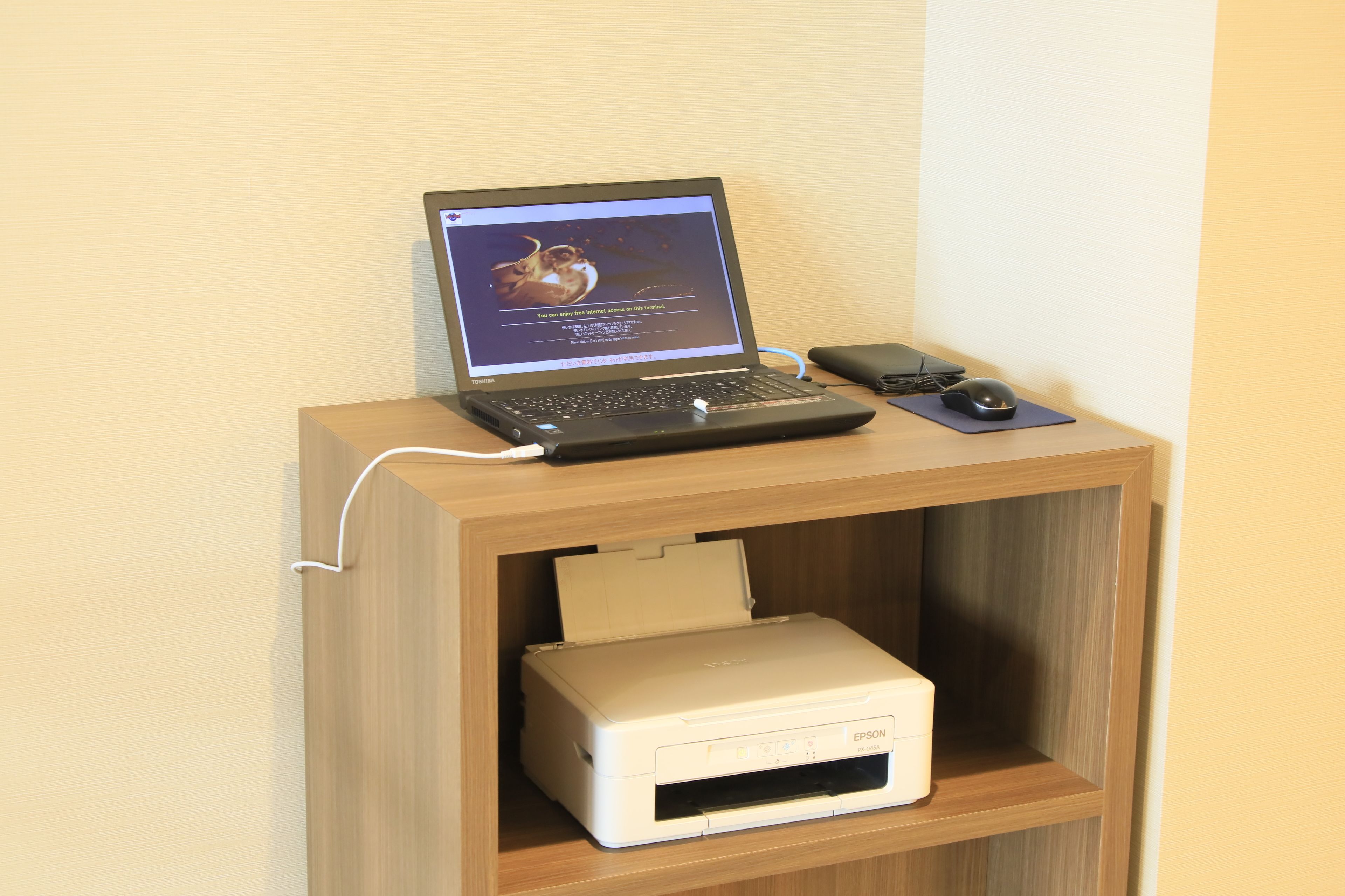 Una computadora portátil sobre una estantería de madera, con una impresora debajo.