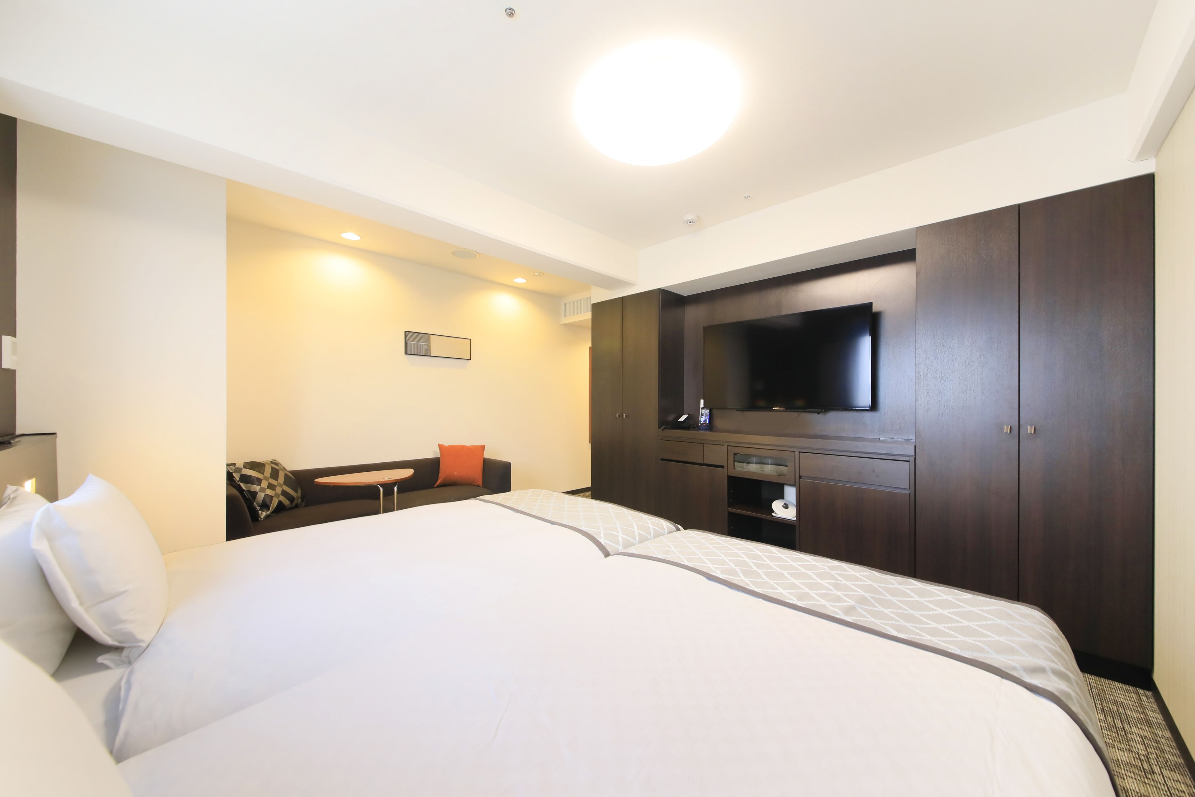 A hotel room with a large bed, a TV mounted on the wall, a small seating area, and a wardrobe.