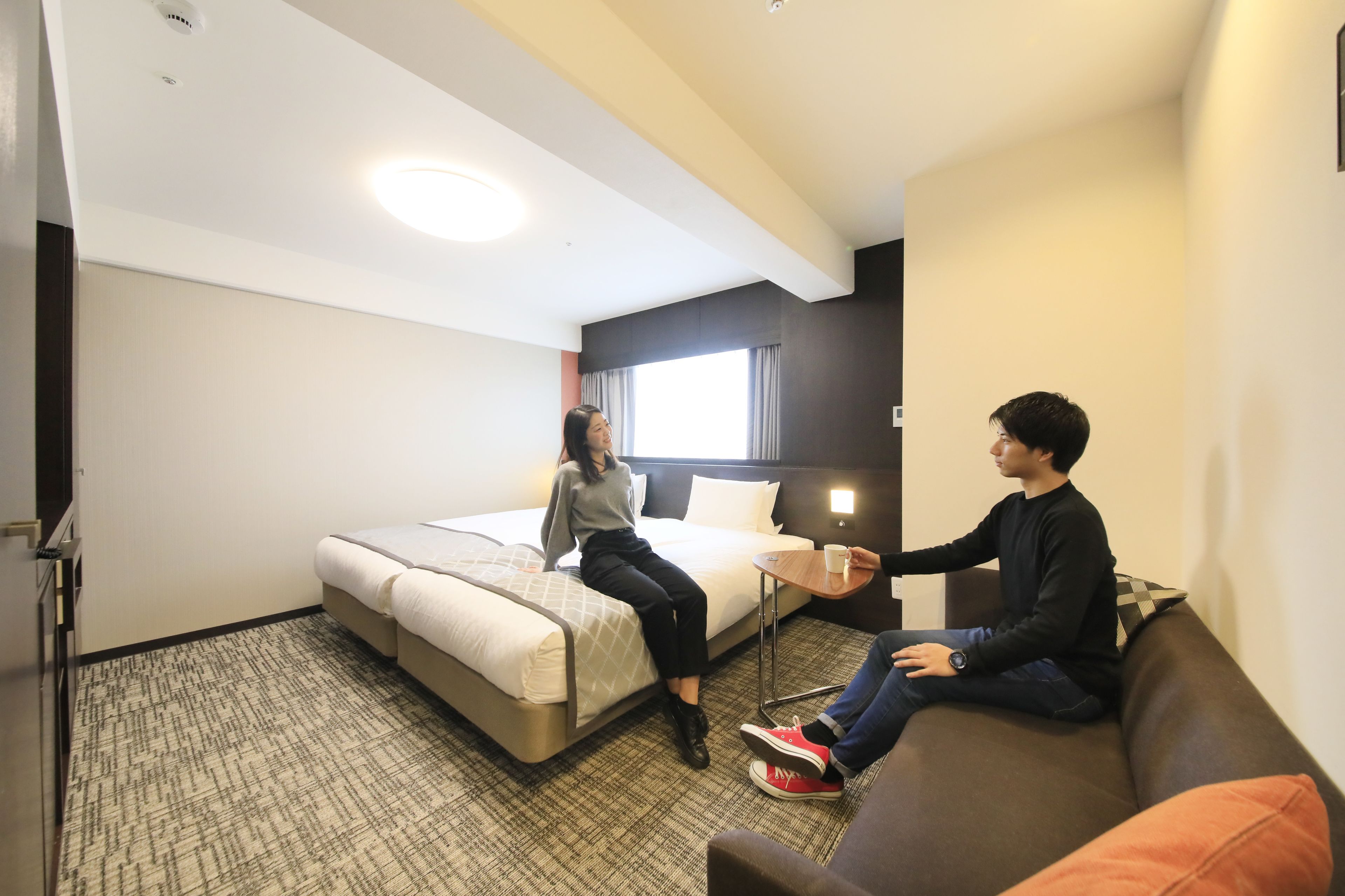A hotel room with a bed, a sofa, a small table, and a window with curtains.