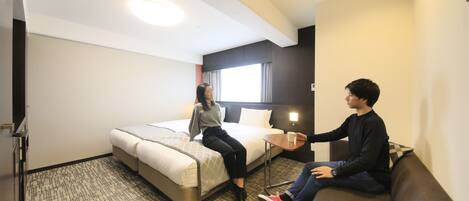 A hotel room with a bed, a sofa, a small table, and a window with curtains.