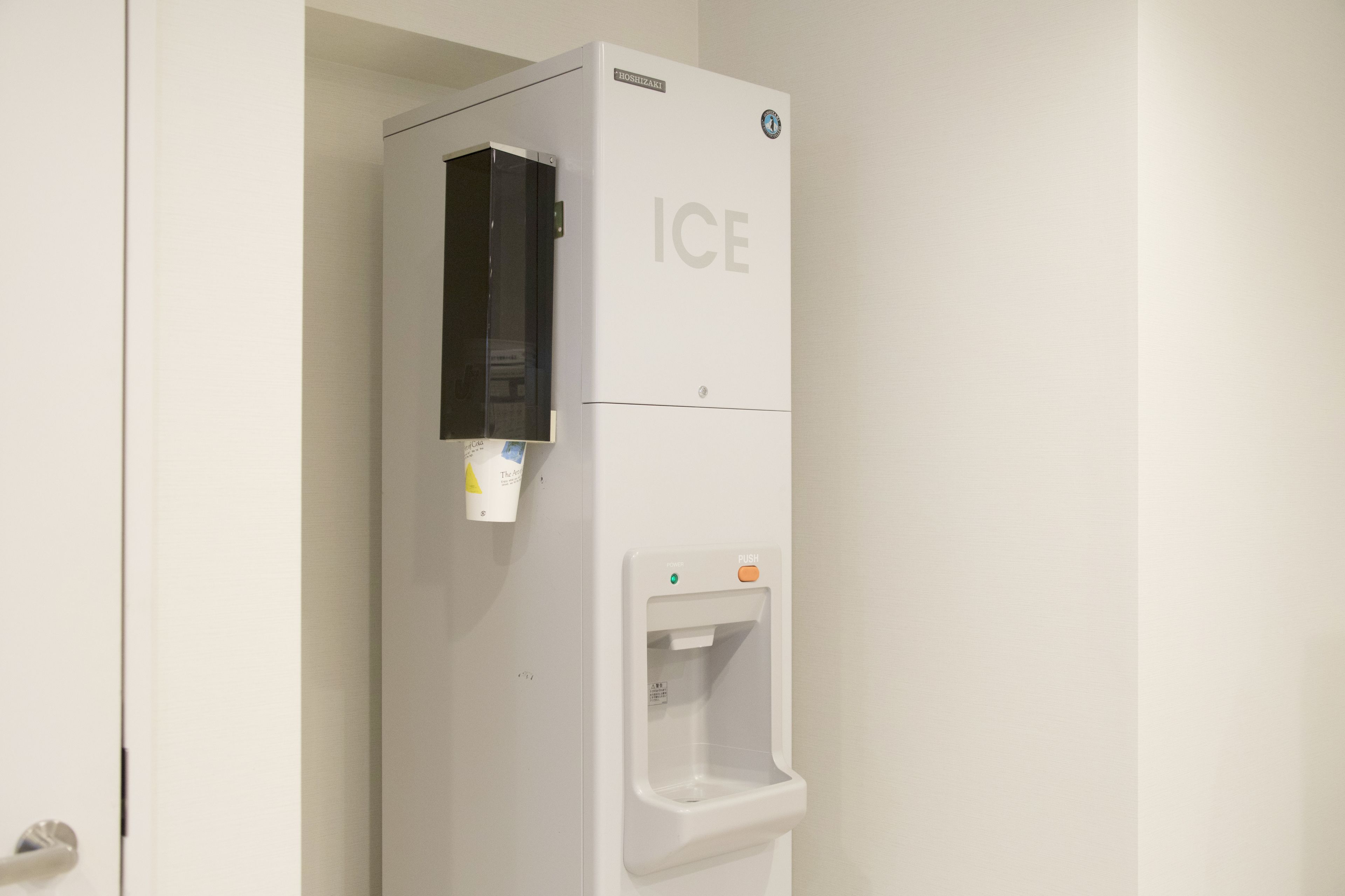 A white ice dispenser with a black panel and a push button.