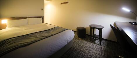 A hotel room with a large bed, a desk, a chair, and a small stool.