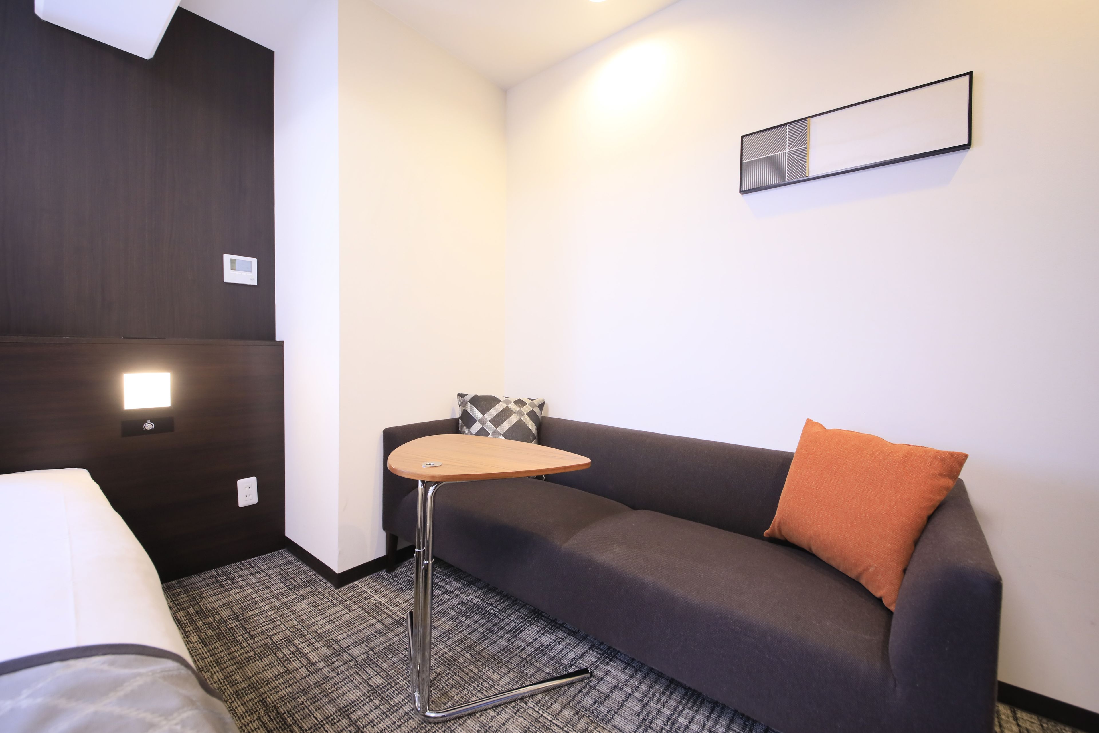 A hotel room with a bed, a sofa, a small table, and a wall-mounted light fixture.