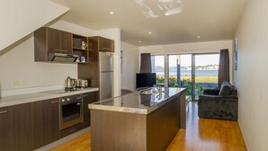 A modern kitchen with a central island, built-in oven, and a large window offering a view of the sea.
