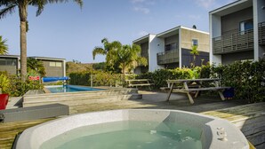A modern outdoor pool area with a hot tub, wooden deck, and adjacent buildings.