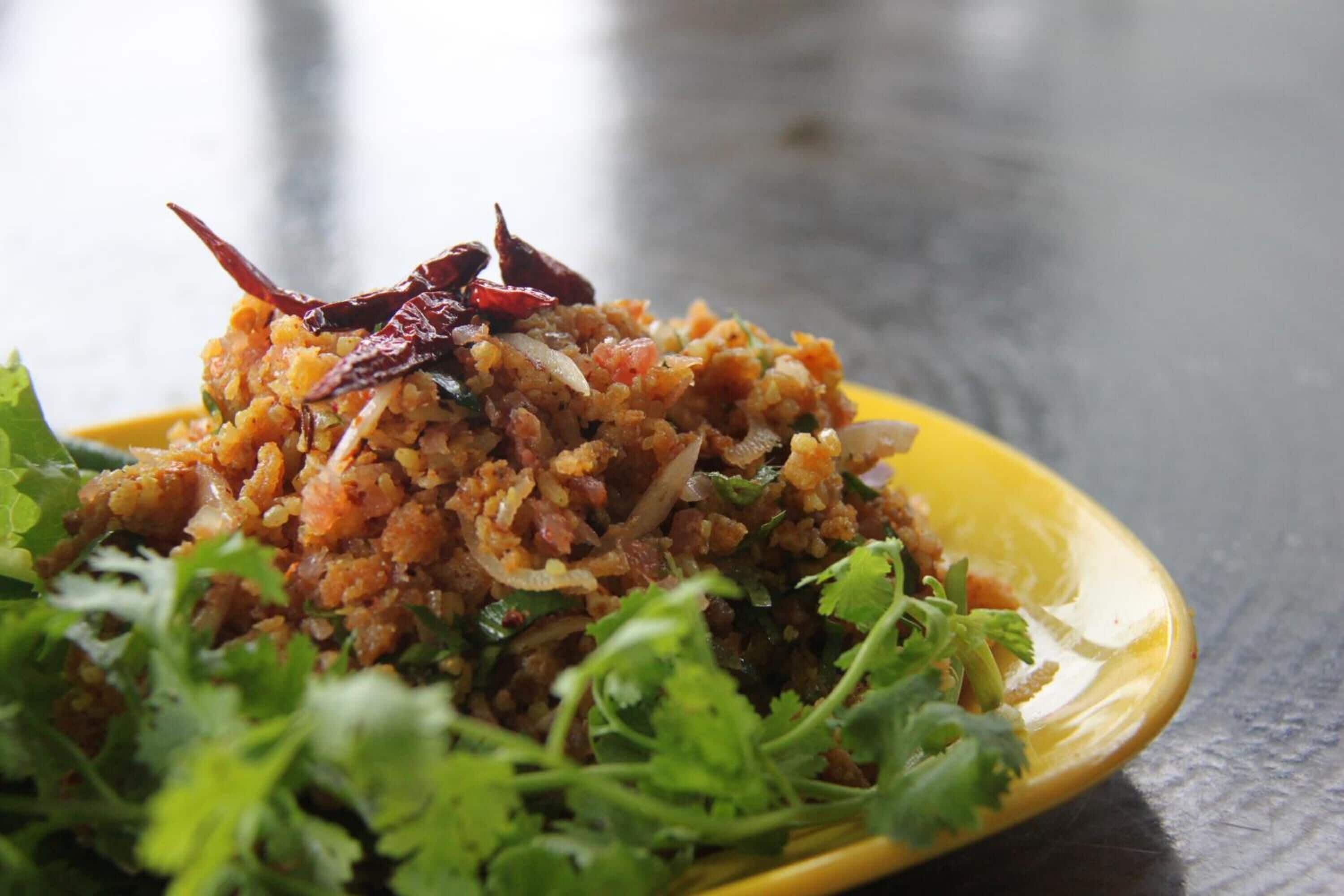 Une assiette jaune contenant un plat de riz mélangé à des herbes et des épices, garni de piments rouges séchés et d’herbes fraîches.