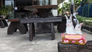 A wooden bench with two white rabbits and a 'WELCOME' sign in front of a building with glass doors. - Cozy Rabbit Hotel (Thung Song)