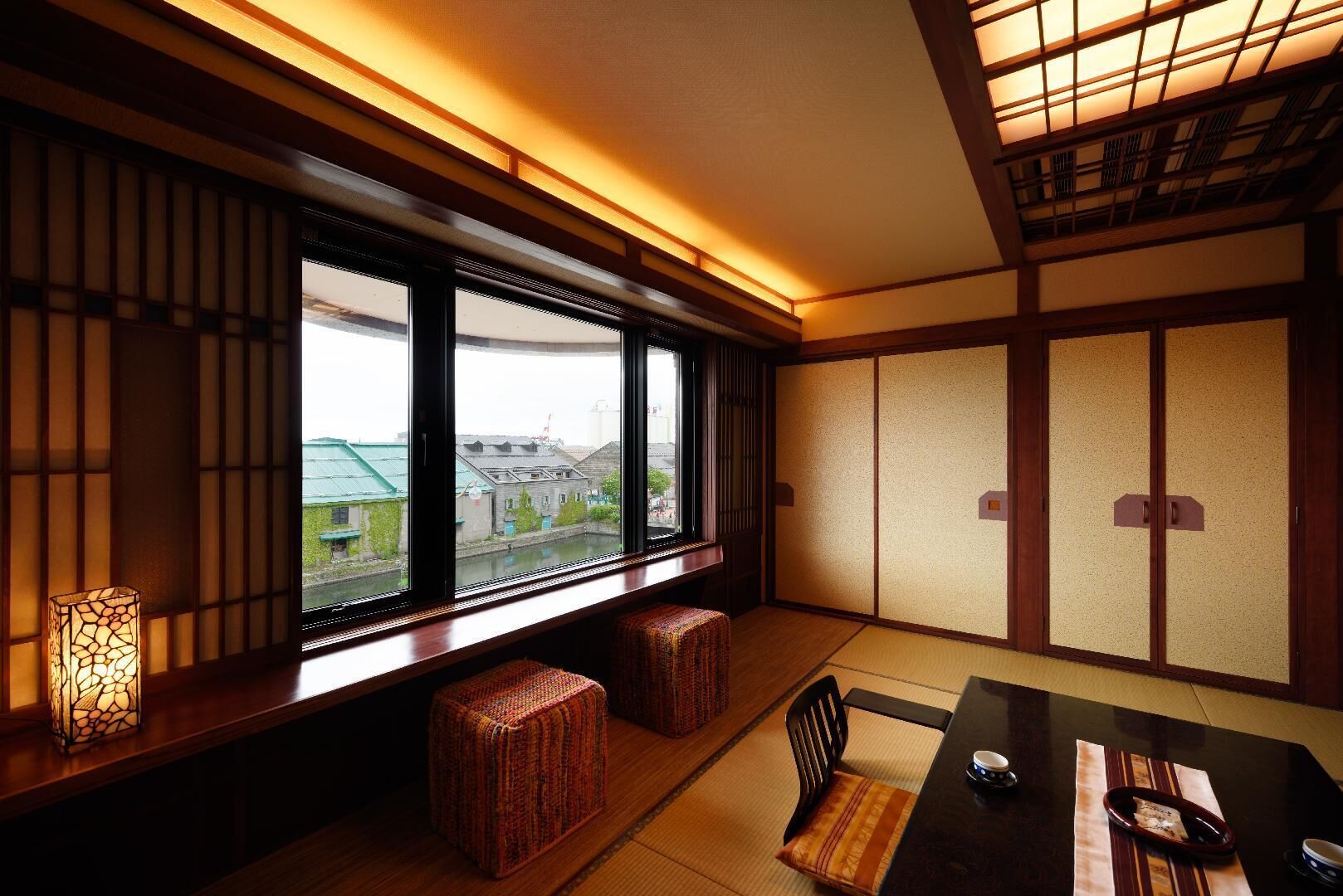 A traditional Japanese room with tatami flooring, a low table, and a view through large windows.