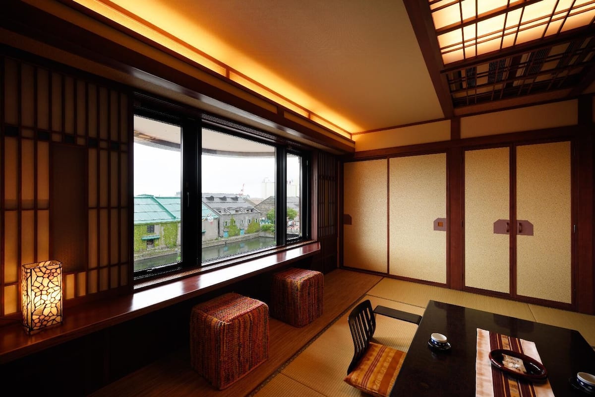 A traditional Japanese room with tatami flooring, a low table, and a view through large windows.