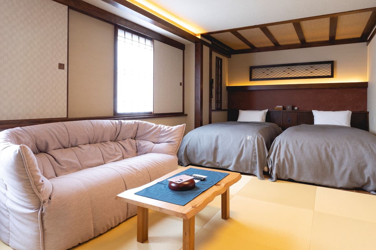 A traditional Japanese-style room with tatami flooring, a low wooden bed, a cushioned sofa, and a small table with a decorative item.
