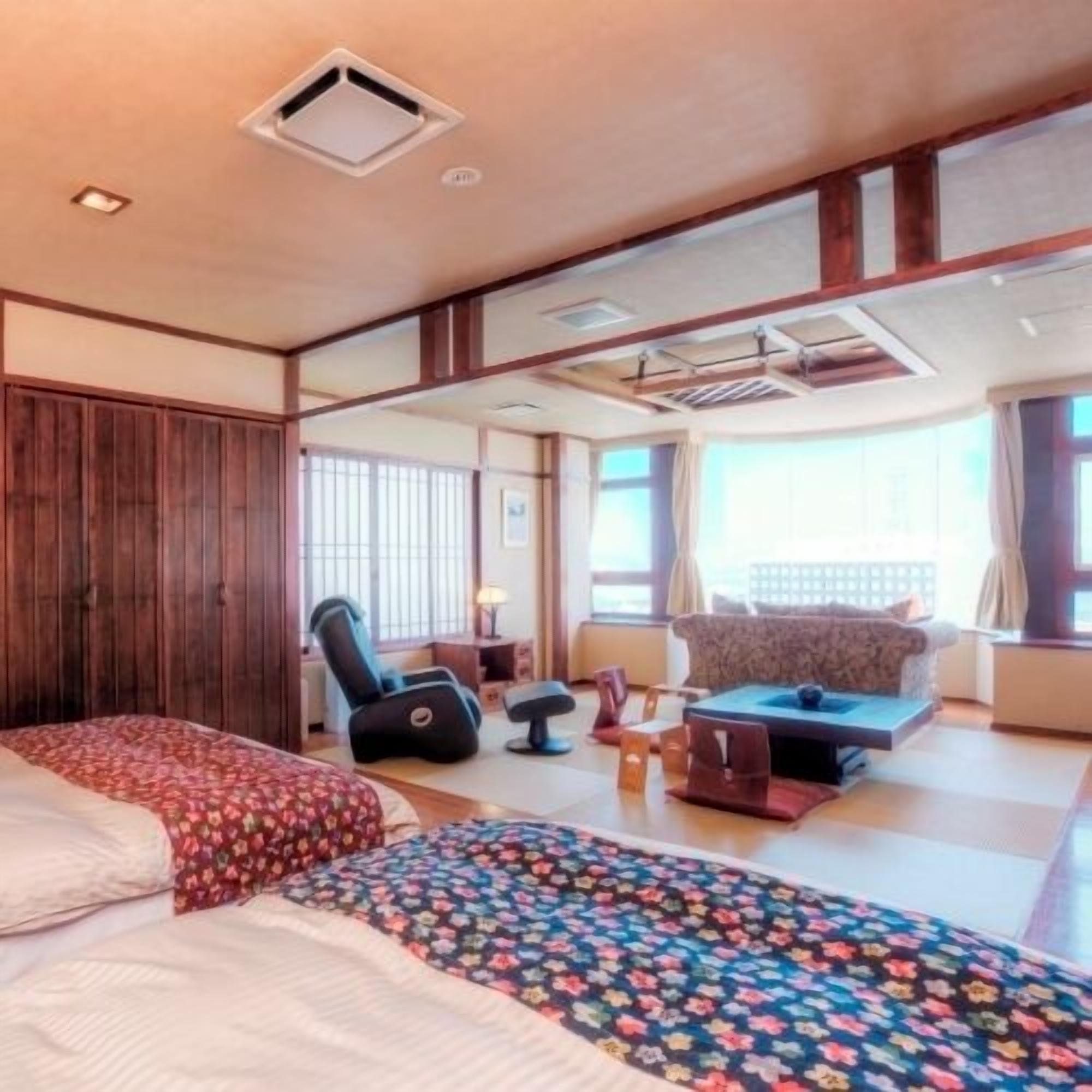 A hotel room with a large bed, a sofa, a massage chair, and a view of the city.