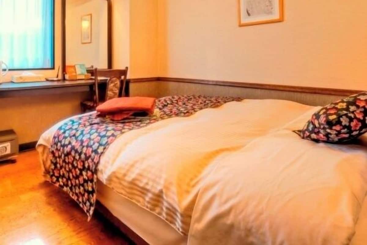 A bedroom with a bed, a window with curtains, a framed picture on the wall, and a wooden headboard.