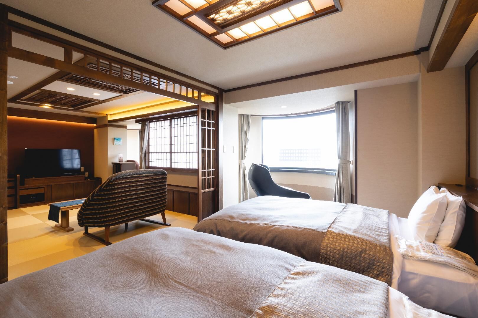 A hotel room with two beds, a television, a desk, and a chair.