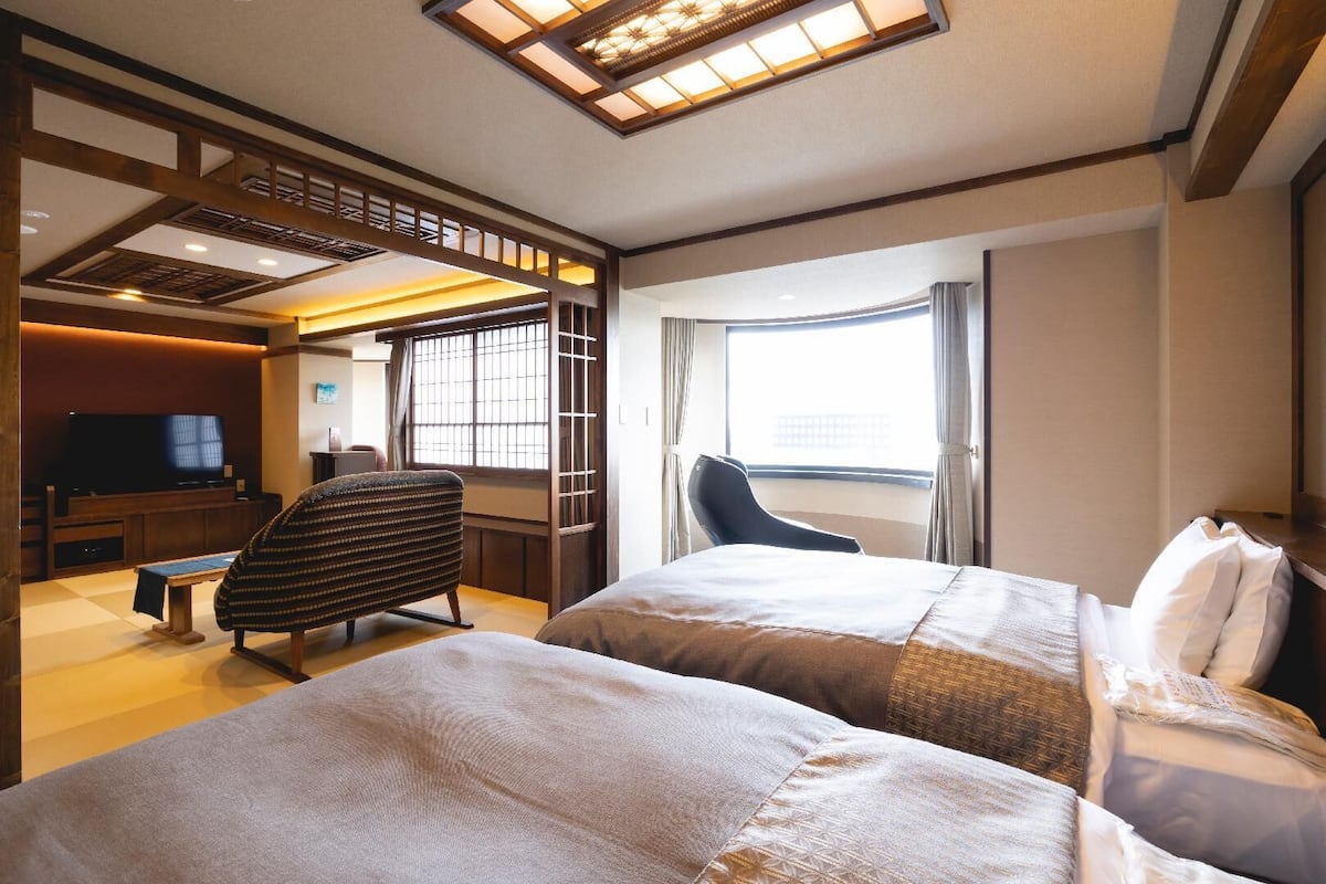 A hotel room with two beds, a television, a desk, and a chair.