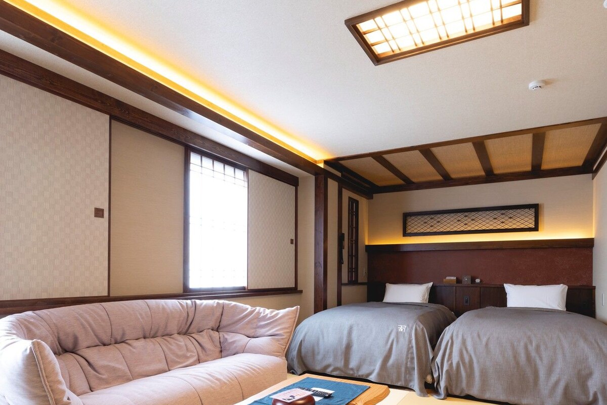 A traditional Japanese-style room with tatami flooring, a low wooden bed, a cushioned sofa, and a small table with a decorative item.