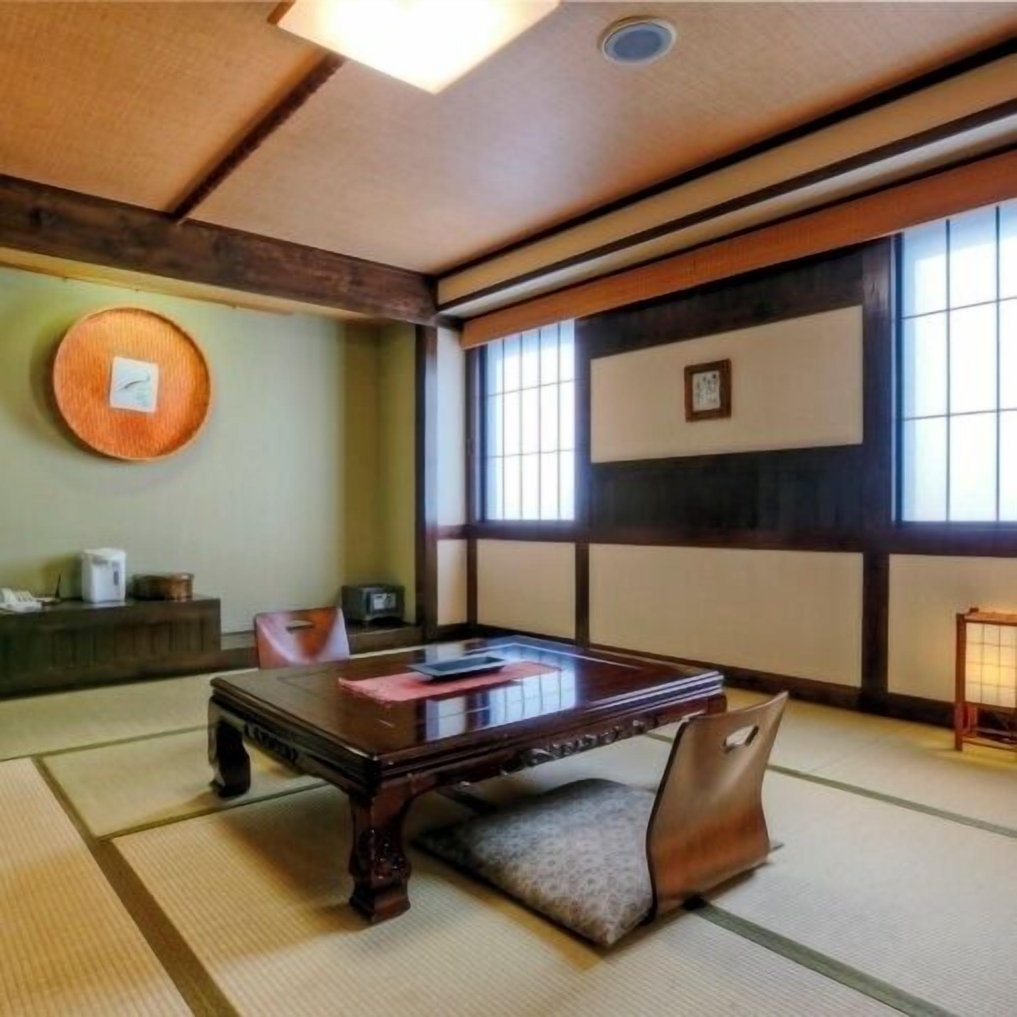 A tatami mat room with a low table, cushions, a wall clock, and a window with a view.