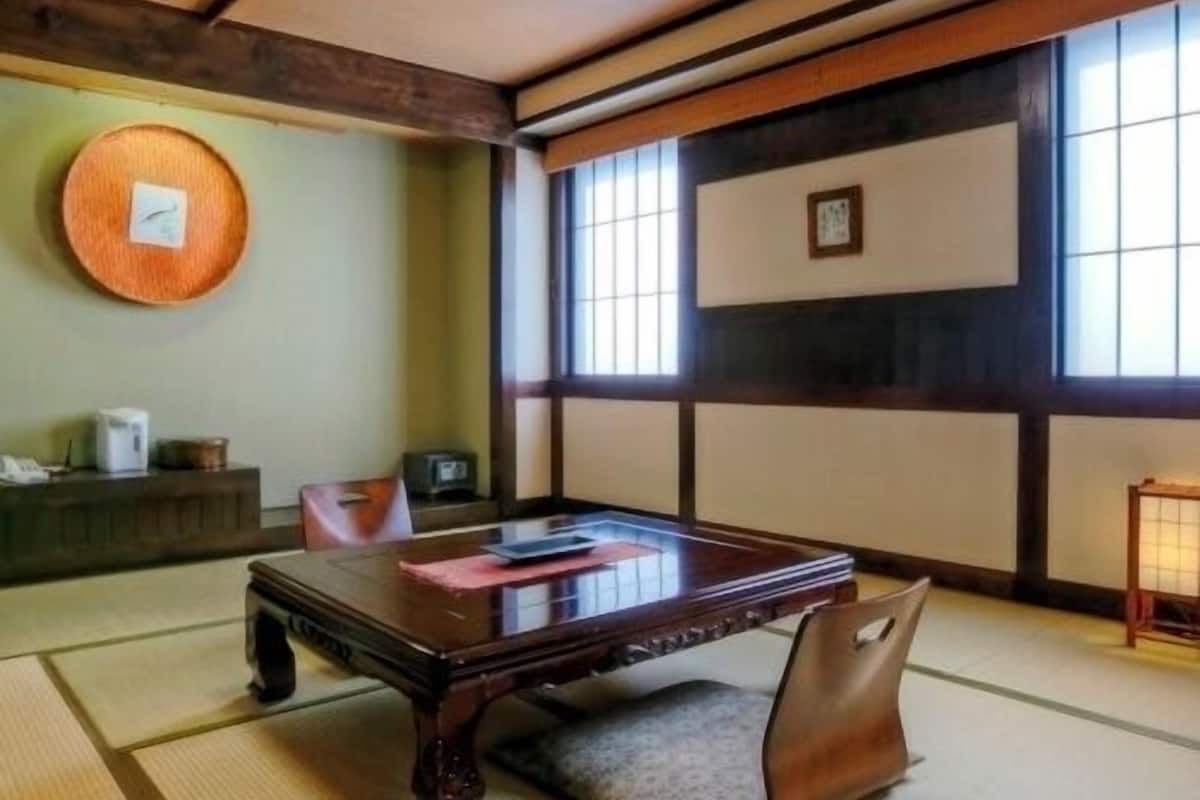 A tatami mat room with a low table, cushions, a wall clock, and a window with a view.
