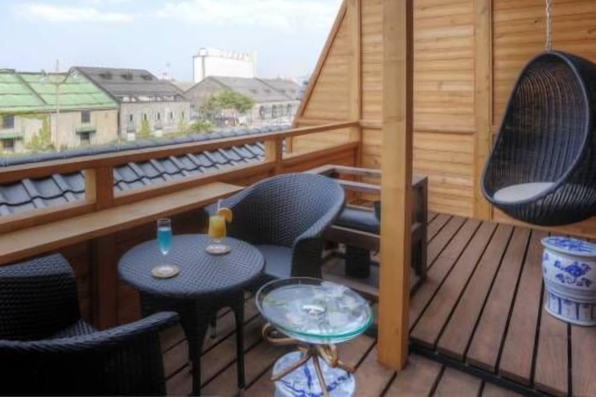 Eine Holzterrasse mit Tisch und Stühlen, einem Hängesessel und Blick auf Gebäude.