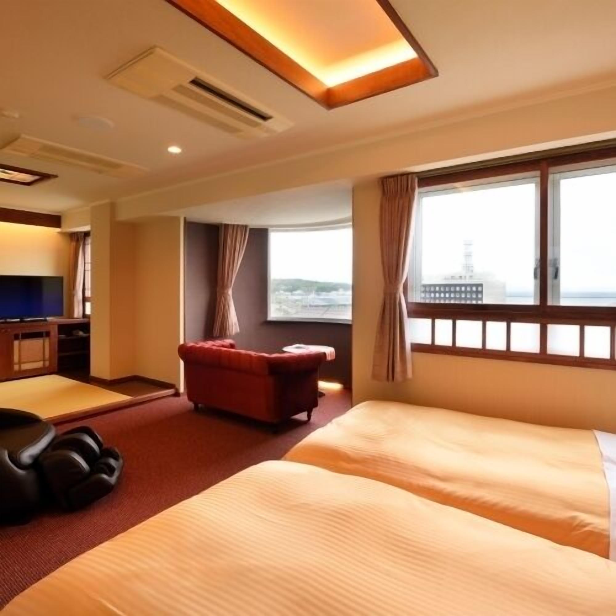A hotel room with a bed, a red armchair, a TV, and a window with a view.