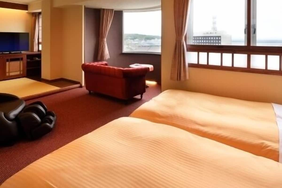 A hotel room with a bed, a red armchair, a TV, and a window with a view.