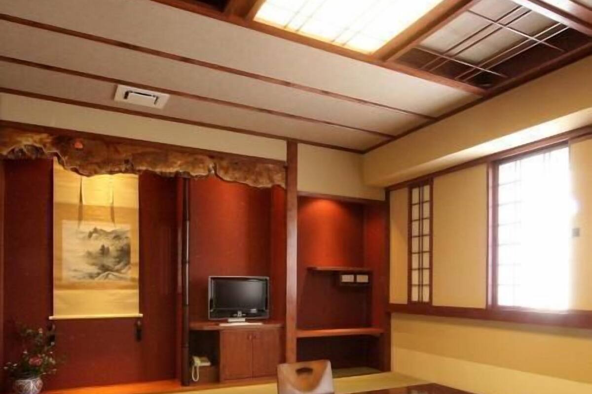 A traditional Japanese room with tatami flooring, a low wooden table, a television, and sliding doors.