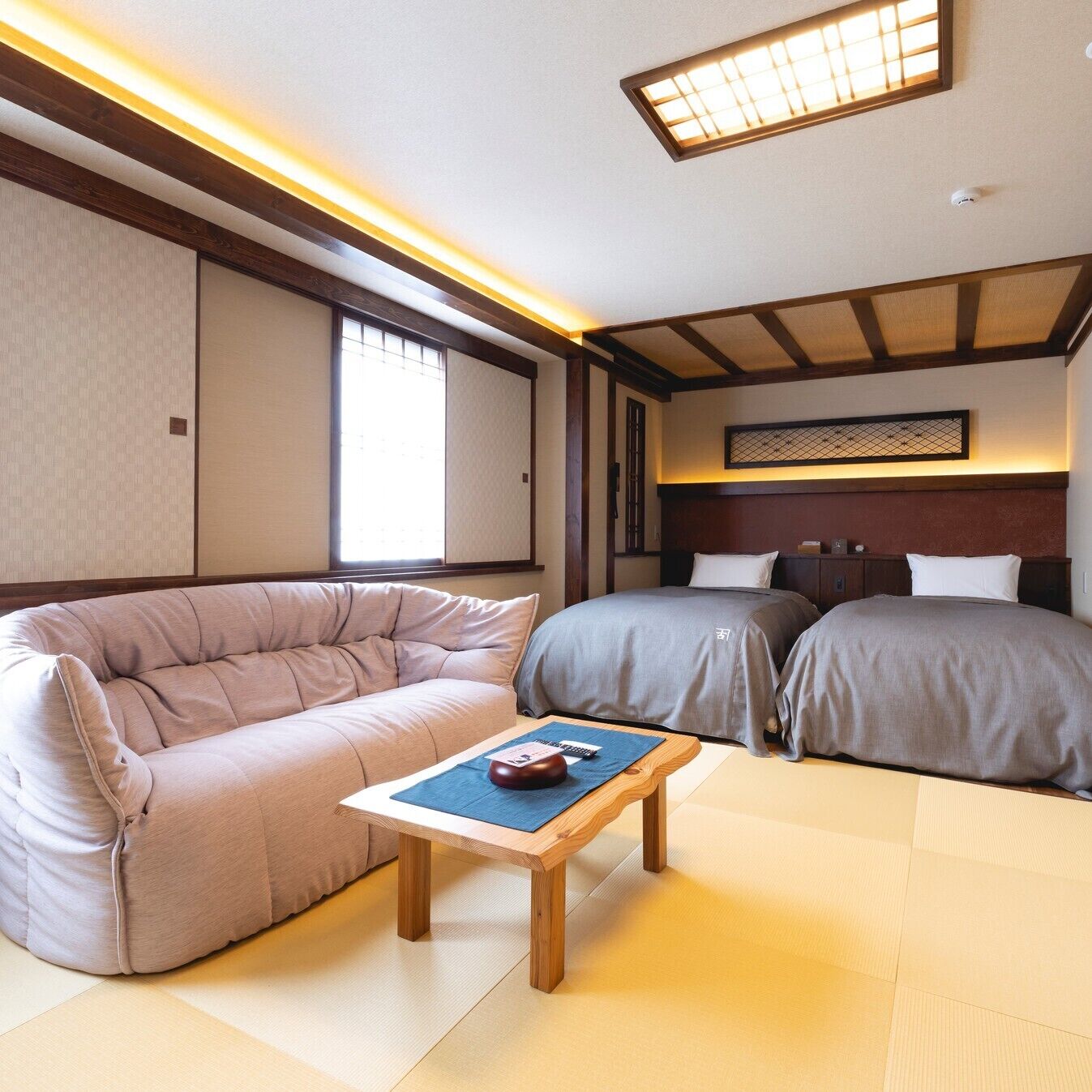 A traditional Japanese-style room with tatami flooring, a low wooden bed, a cushioned sofa, and a small table with a decorative item.