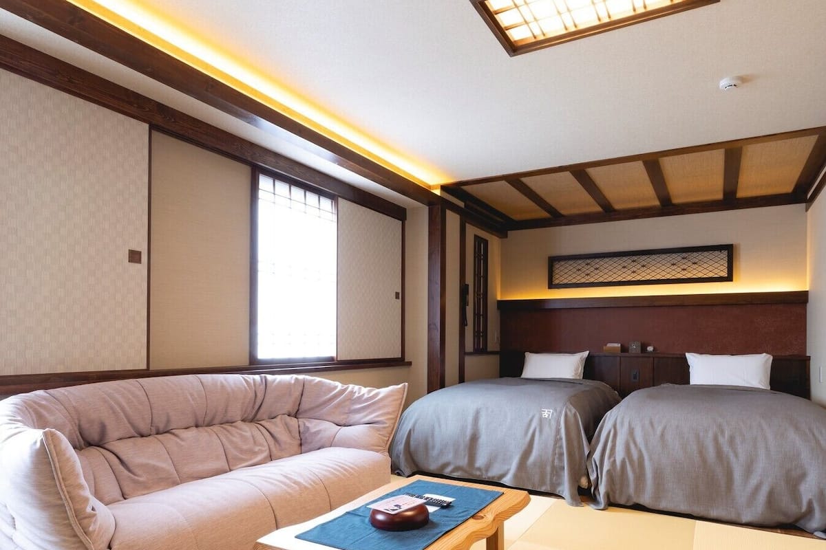 A traditional Japanese-style room with tatami flooring, a low wooden bed, a cushioned sofa, and a small table with a decorative item.